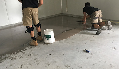 Two installers applying a slurry mix to level and flatten a floor.