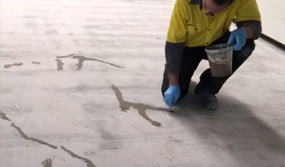 An installer using a patching compound to repair small static cracks in a concrete slab.