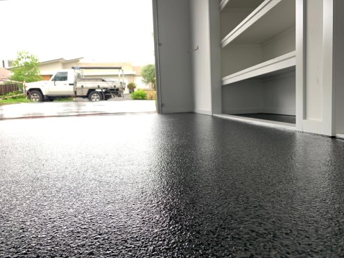 A low-angle photo showing a beautiful, even finish on a black epoxy flake garage floor.
